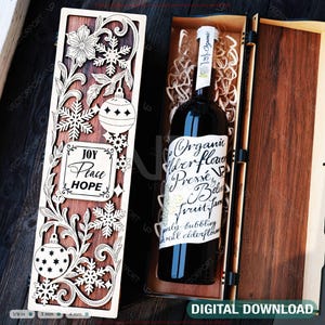 Può includere: Una scatola di vino in legno con intricati disegni tagliati al laser di fiocchi di neve, ornamenti e motivi floreali. La scatola contiene una bottiglia di vino con un'etichetta che recita "Organic Elderflower Presse". Sono visibili anche le parole "Joy, Peace, Hope".