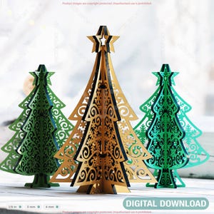 May include: Three decorative Christmas trees in gold and green, with intricate cut-out designs. The trees are arranged on a white surface, with a window in the background. The text "DIGITAL DOWNLOAD" is visible.
