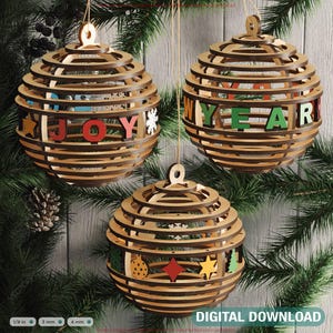 Op de afbeelding: Drie houten kerstballen met een gelaagd ontwerp, hangend aan een groene dennentak. Eén bal spelt "JOY" in kleurrijke letters, een andere zegt "NEW YEAR", en de derde heeft feestelijke vormen. De woorden "DIGITALE DOWNLOAD" staan onderaan.