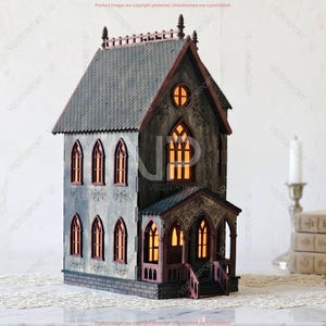 May include: A detailed, miniature haunted house model with a gray facade, dark roof, and arched windows. The windows glow with an orange light, suggesting an interior light source. The house has a porch and is set on a decorative surface.