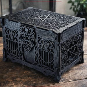 May include: Black wooden box with intricate gothic-style carvings. The box features a pentagram design on the lid and sides, along with skull and floral accents. The box is rectangular and sits on four small feet.