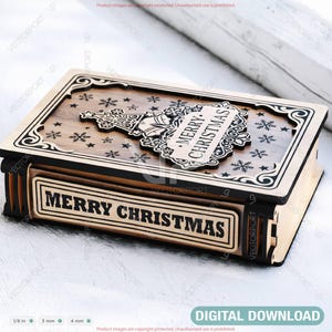May include: A wooden Christmas box with a decorative lid featuring a laser-cut Christmas tree and snowflakes. The box has the words "MERRY CHRISTMAS" on the front and lid. The box is made of light brown wood with black accents.