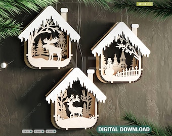 Könnte beinhalten: Set aus drei lasergeschnittenen Weihnachtsanhängern aus Holz. Jeder Anhänger ist in Form eines Hauses mit einem schneebedeckten Dach und einem Fenster mit einer anderen Winterszene gestaltet. Der erste Anhänger zeigt einen Elch in einem Wald, der zweite einen Schneemann und ein Haus und der dritte ein Rentier in einem Wald.