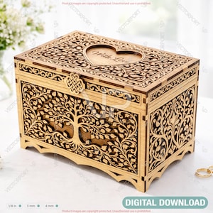 May include: A wooden box with intricate laser-cut designs, including a tree of life and floral patterns. The lid features a heart-shaped cutout with the words "With Love." The box is light brown and has a clasp closure. Two gold rings are visible.