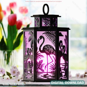 Puede incluir: Linterna de madera negra con un diseño de flamenco rosa. La linterna tiene un panel de vidrio transparente y un brillo rosa que proviene del interior. La linterna está sentada en una mesa con un jarrón de flores rosas en el fondo.