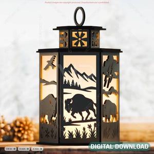 May include: Black laser-cut lantern with a handle, featuring bison, mountains, and birds. The lantern has a decorative top and sides with cut-out designs. The lantern is approximately 6 inches tall and is designed to hold a light source.
