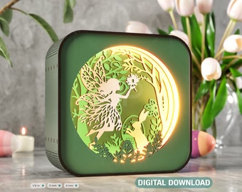 Pode incluir: Uma luz noturna de madeira verde com uma fada e um coelho em uma cena de floresta. A luz é iluminada por trás, criando um brilho quente. O texto "DOWNLOAD DIGITAL" está na parte inferior da imagem.