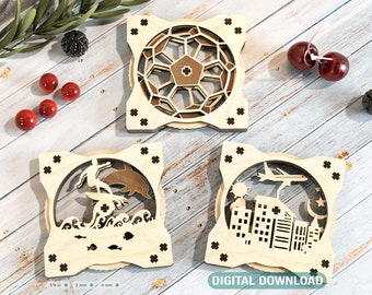 May include: Three wooden laser cut ornaments with intricate designs. The first ornament features a geometric pattern, the second a surfer riding a wave with a dolphin, and the third a cityscape with a plane flying overhead. The ornaments are on a light wood background.