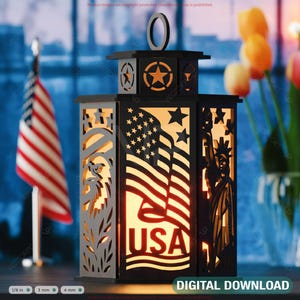 May include: Black wooden lantern with cut-out designs of the American flag, Statue of Liberty, and an eagle. The word "USA" is visible. The lantern has a handle and a star design on top. A small American flag is in the background.