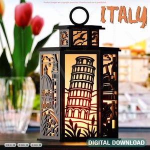 May include: A black wooden lantern with a cutout design of the Leaning Tower of Pisa and other Italian landmarks. The lantern is lit from within, casting a warm glow. The text "ITALY" is visible at the top of the image.