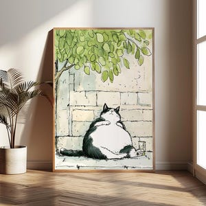 May include: A framed art print featuring a watercolor illustration of a relaxed, black and white cat. The cat is sitting against a brick wall under a tree with green leaves. A glass of liquid sits beside the cat. The artwork is in a wooden frame.