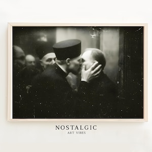 Puede incluir: Fotografía vintage en blanco y negro de dos hombres besándose, con otros en el fondo. La imagen está enmarcada en un marco de madera clara. El texto "NOSTALGIC ART VIBES" está en la parte inferior.
