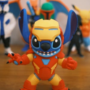 May include: A colorful figurine of Stitch in an Iron Man suit. The figure is primarily red, yellow, and blue, with black claws and a yellow helmet. Other figurines are visible in the background.