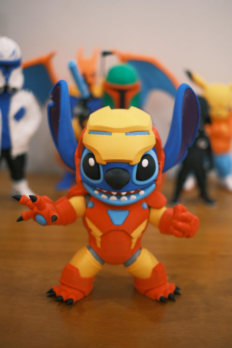 May include: A colorful figurine of Stitch in an Iron Man suit. The figure is primarily red, yellow, and blue, with black claws and a yellow helmet. Other figurines are visible in the background.