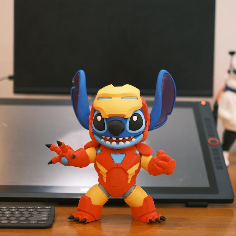 May include: A figurine of Stitch, the Disney character, in an Iron Man suit. The figure is primarily red and yellow, with blue ears and head. The figure is posed with its arms out, and has a smiling expression.
