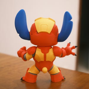 May include: A red, yellow, and blue figurine of a character with large ears. The figurine has a robotic appearance, with yellow accents on the chest, head, and legs. The character's ears are blue, and it has black claws.