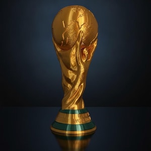 May include: A gold-colored trophy featuring two human figures with raised arms supporting a globe at the top. The base is circular with a green band and the embossed text FIFA WORLD CUP. The design has a metallic finish and reflective surface.