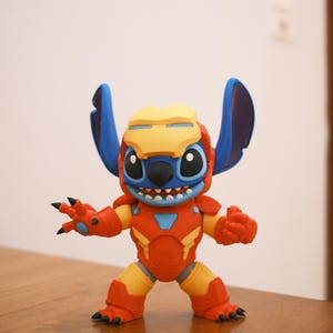 May include: A figurine of Stitch, the blue alien from Lilo & Stitch, in an Iron Man-inspired suit. The figure is primarily red and yellow, with blue ears and a yellow helmet. The figure has a smiling expression.