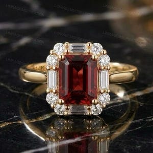 Könnte beinhalten: Ein 14k Goldring mit einem großen, rechteckigen, smaragdgeschliffenen tiefroten Edelstein in der Mitte. Der Stein ist von einem Heiligenschein aus kleinen, runden, im Brillantschliff geschliffenen weißen Diamanten und vier Baguette-Diamanten umgeben.