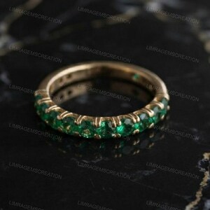 Könnte beinhalten: Ein Goldring mit einer durchgehenden Reihe von rund geschliffenen, leuchtend grünen Edelsteinen in einer gemeinsamen Krappenfassung. Der Ring hat eine polierte metallische Oberfläche und ein gleichmäßiges kreisförmiges Design mit grünen Steinen.