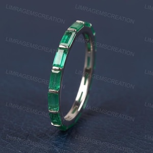 Peut inclure: Une bague en argent ornée de pierres précieuses vertes taille émeraude. La bague présente une ligne continue d'émeraudes rectangulaires, rapprochées pour un aspect vibrant et élégant. Les pierres sont d'un vert profond.