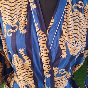 May include: Blue and gold tiger print robe with white trim. The robe features a striped pattern with tiger illustrations. The robe has pockets and a belt. The robe is displayed on a mannequin.