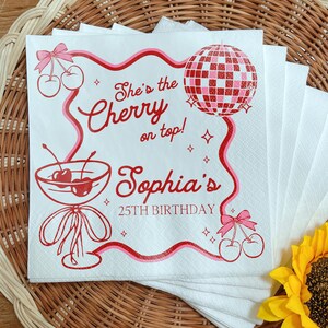 May include: White paper napkins with a red and pink design. The design includes cherries, a disco ball, and the text "She's the Cherry on top! Sophia's 25th Birthday."