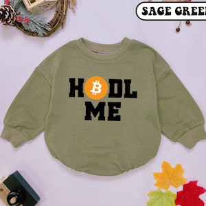 May include: Sage green long-sleeve sweatshirt with a black graphic that says "HODL ME" and features a yellow Bitcoin symbol.