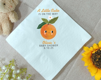 Könnte beinhalten: Eine weiße quadratische Serviette mit dem Text "A Little Cutie is on the Way" und "Olivia's Baby Shower 6.10.25". Die Serviette zeigt eine Cartoon-Orange mit lächelndem Gesicht, Blättern und einer weißen Blume.
