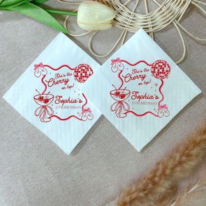 May include: Two white square napkins with a red cherry and disco ball design. The text reads "She's the Cherry on top! Sophia's 25th Birthday". The napkins are folded and placed on a neutral surface.