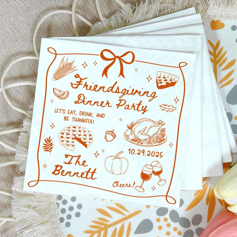 May include: White Friendsgiving dinner party napkins with an orange border and illustrations. The napkins feature text that reads "Friendsgiving Dinner Party" and "Let's eat, drink, and be thankful!" with the date 10.29.2025.