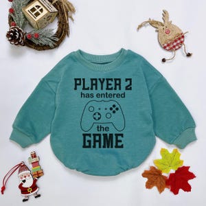 May include: A teal blue long-sleeved sweatshirt with a black graphic of a video game controller and the text "PLAYER 2 has entered the GAME".