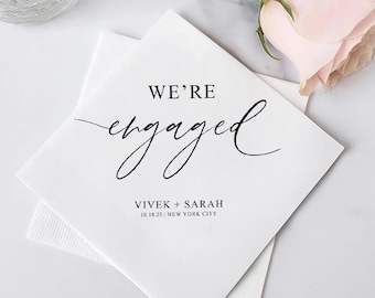 May include: White square napkins with the words "WE'RE engaged" in black script. Below the text are the names "Vivek + Sarah" and the date and location "10.18.25 | NEW YORK CITY". A pink rose is in the background.
