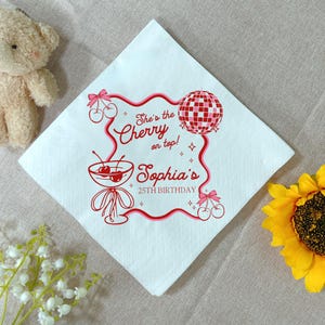 May include: White square paper napkin with a red and pink design. The design includes a cocktail glass with cherries, a disco ball, and text that reads "She's the Cherry on top! Sophia's 25th Birthday."