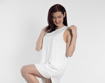 May include: A white sleeveless dress with a relaxed fit and a slightly frayed hem. The dress is worn by a person with dark hair and is paired with white sneakers.