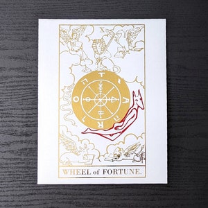 May include: A tarot card with a gold background and a red and white illustration of a wheel of fortune. The card is titled "WHEEL of FORTUNE."