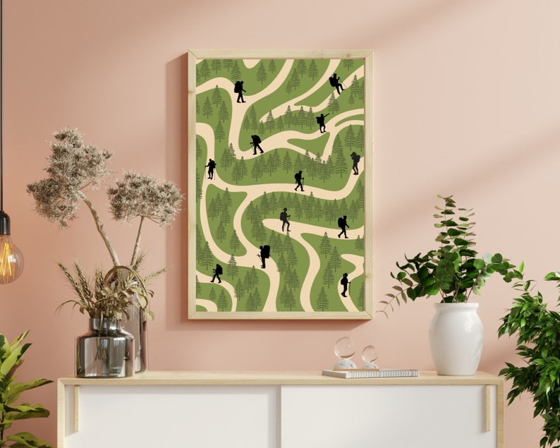 May include: A framed print with a green and cream background featuring a winding path through a forest. Silhouettes of hikers are walking along the path.