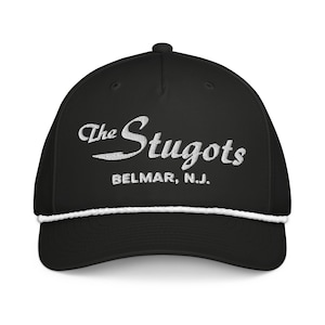 May include: Black baseball cap with white embroidered text "The Stugots" and "BELMAR, N.J.". The cap has a white rope detail along the brim. A stylish and comfortable accessory for everyday wear.