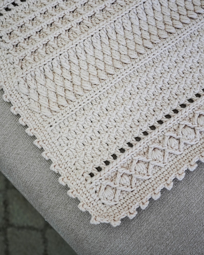 Peut inclure: Gros plan sur une couverture au crochet de couleur beige avec un bord festonn&eacute;. La couverture pr&eacute;sente un motif textur&eacute; avec un motif r&eacute;p&eacute;titif.