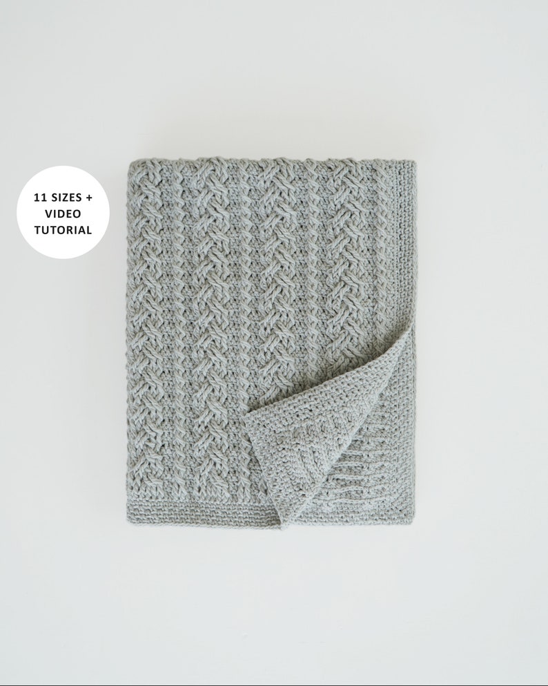 May include: A gray crocheted blanket with a woven pattern. The blanket is folded in half and the edges are visible. The text "11 SIZES + VIDEO TUTORIAL" is in a white circle in the top left corner of the image.