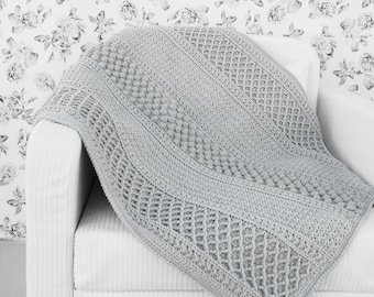 Puede incluir: Una manta de punto de ganchillo gris con un patrón texturizado, drapeada sobre un sillón blanco.