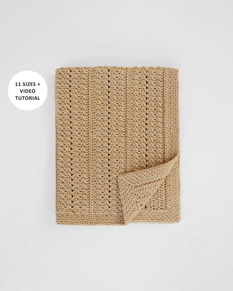 May include: A folded, beige crochet blanket with a textured stitch pattern. The blanket has a rectangular shape with a folded corner, revealing the detailed edge. The text "11 SIZES + VIDEO TUTORIAL" is in a white circle in the upper left corner.