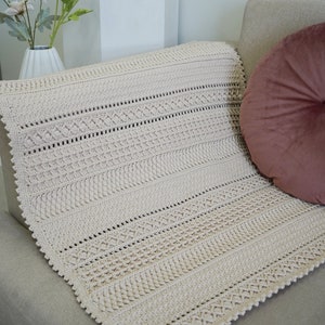 Peut inclure: Une couverture en crochet beige avec un motif textur&eacute;, pos&eacute;e sur un canap&eacute; brun clair avec un coussin rose.