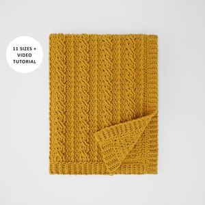 Puede incluir: Una manta de crochet de color amarillo mostaza con un patrón de punto de cable. La manta está doblada por la mitad y el texto "11 SIZES + VIDEO TUTORIAL" es visible en un círculo blanco.