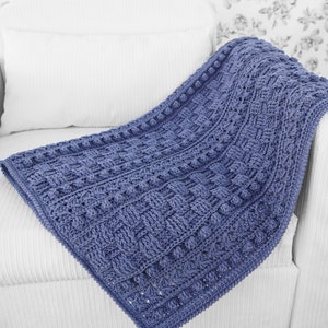 May include: A blue crocheted blanket with a textured pattern and a raised border. The blanket is draped over a white armchair.
