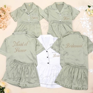 Op de afbeelding: Saliegroene satijnen pyjamasets met witte biezen, geborduurd met namen en titels als "Sherry", "Tori", "Maid of Honor" en "Bridesmaid". Een witte pyjamaset met "Bride" is ook inbegrepen.