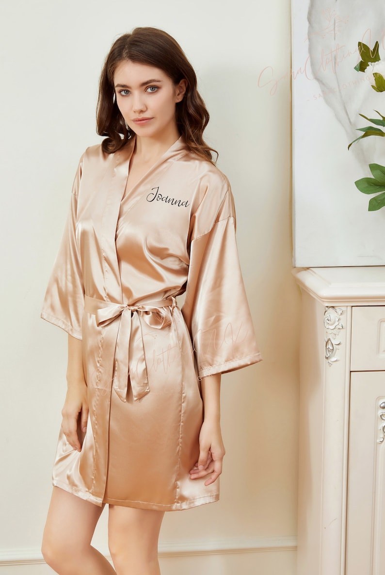 May include: A gold satin robe with a black embroidered name "Joanna" on the left side of the chest.