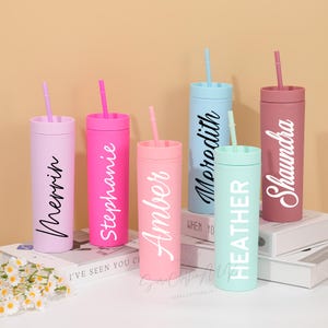 Könnte beinhalten: Sechs personalisierte Becher in Pastellfarben, jeweils mit passendem Strohhalm. Die Becher sind mit Namen in einer stilvollen Schriftart beschriftet. Die Farben umfassen Rosa, Lila, Blau und Grün.