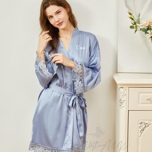 May include: A light blue satin robe with lace trim on the sleeves and hem. The robe has a white embroidered name "Alan" on the front.