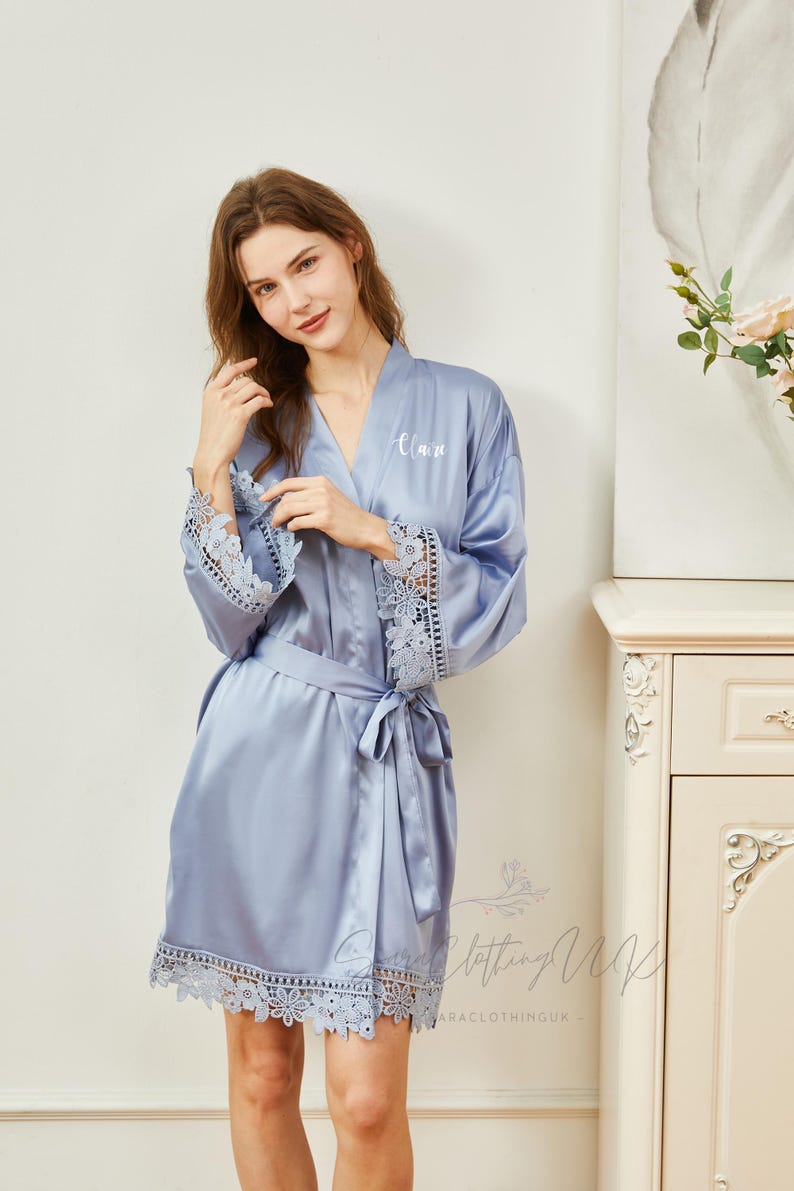 May include: A light blue satin robe with lace trim on the sleeves and hem. The robe has a white embroidered name "Alan" on the front.